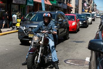 A man rides a motorcycle down a crowded street in Union City, NJ with cars behind him.
